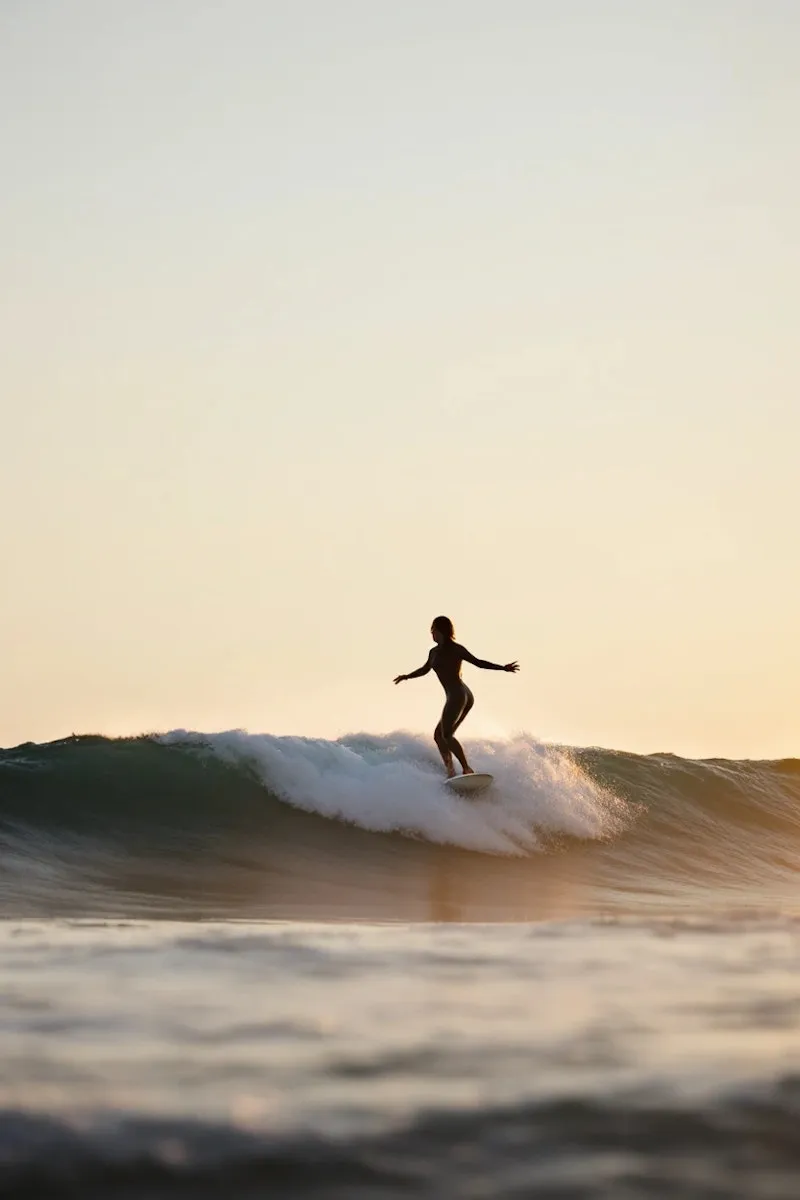 Silhouette of surfer balancing on a wave during sunset