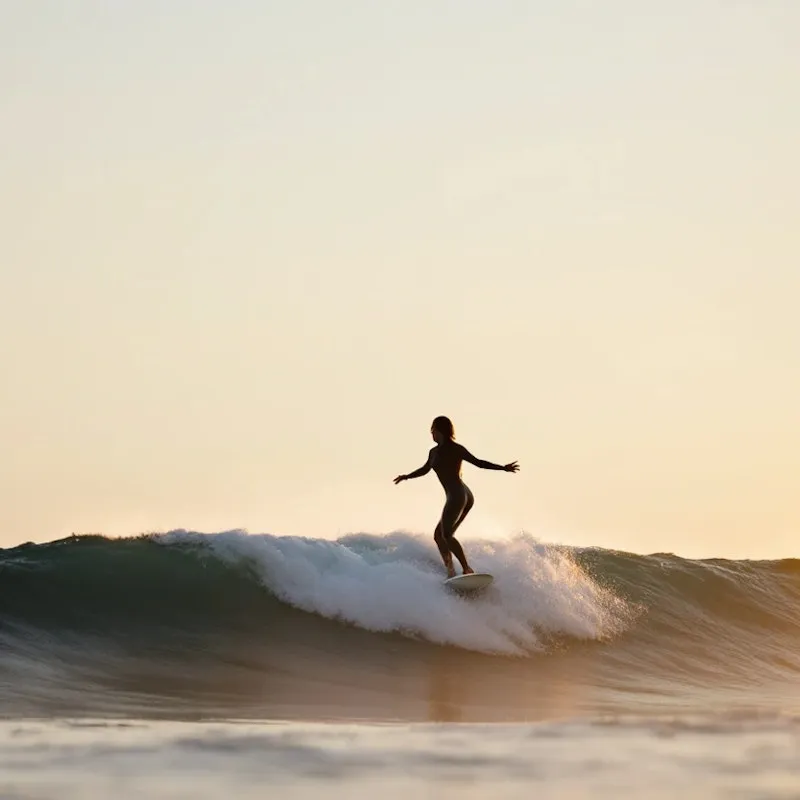 Silhouette of surfer balancing on a wave during sunset